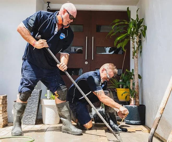 Plumbers clearing a drain at a front door